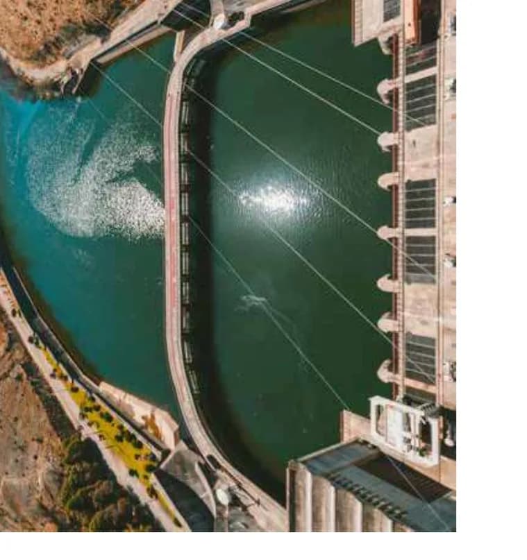 Vista aérea de barragem e reservatório, com vertedouro em operação e estrutura de contenção em concreto